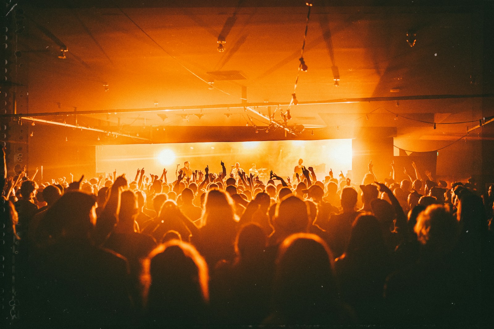 A packed concert crowd silhouetted against bright amber stage lights